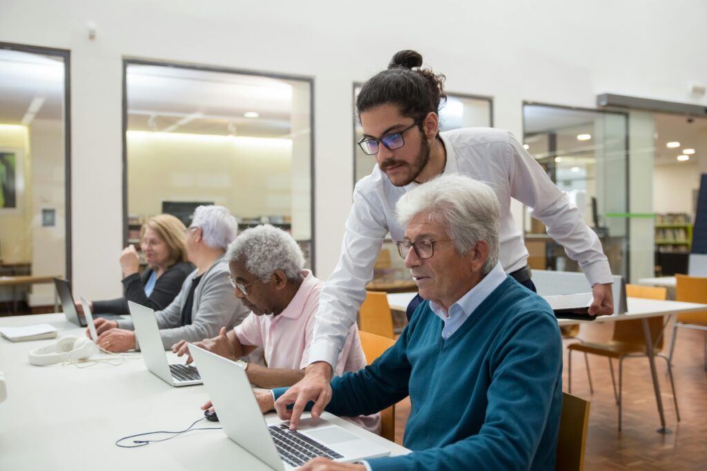A teacher guiding senior adults in a library, using laptops for learning and support.
